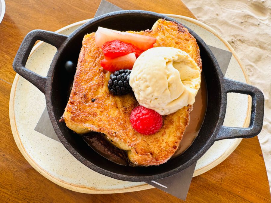 A huge slice of French toast atop a bed of caramel sauce, topped with fresh berries and vanilla ice cream.