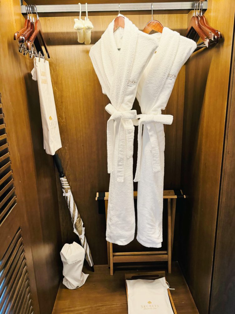 Photo of teak closet at all-inclusive Impression Moxché resort in Playa Del Carmen, Mexico. Two luxurious bathrobes, slippers, an umbrella and a steam-iron are shown within the closet.