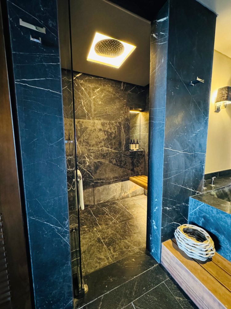 Photo of an oversized black granite walk-in shower with glass door, found in the guest suite at all-inclusive Impression Moxché in Playa Del Carmen, Mexico.