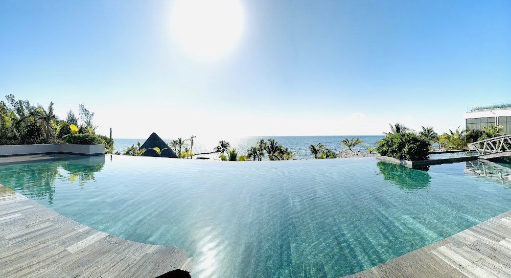Infinity edge rooftop pool overlooking the ocean on a beautiful, sunny, sky-blue day. the water is aqua blue and the ocean is in the distance.