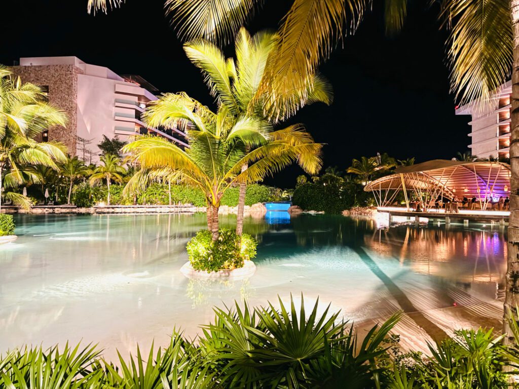 Nighttime view of the main pool area at Impressions Moxché all-inclusive resort with beautiful lighting and bright green foliage.