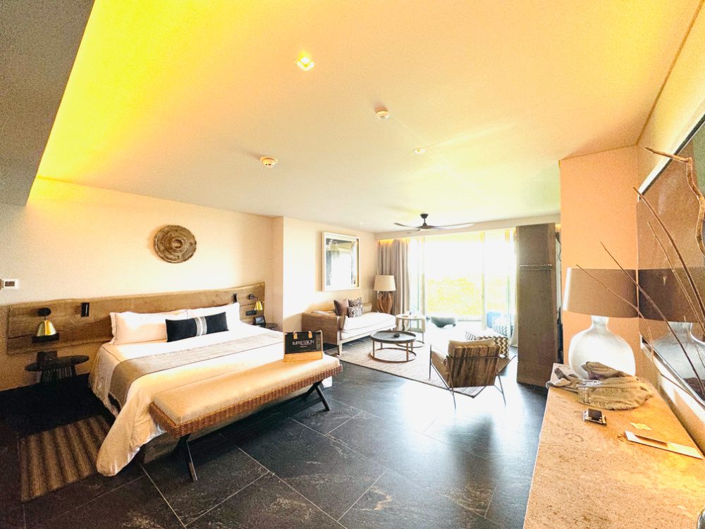 Bedroom and living area in the guest suite at Impression Moxché includes an oversized King bed and a living room seating area as well as a small refrigerator, snack bar and entertainment / tv area.